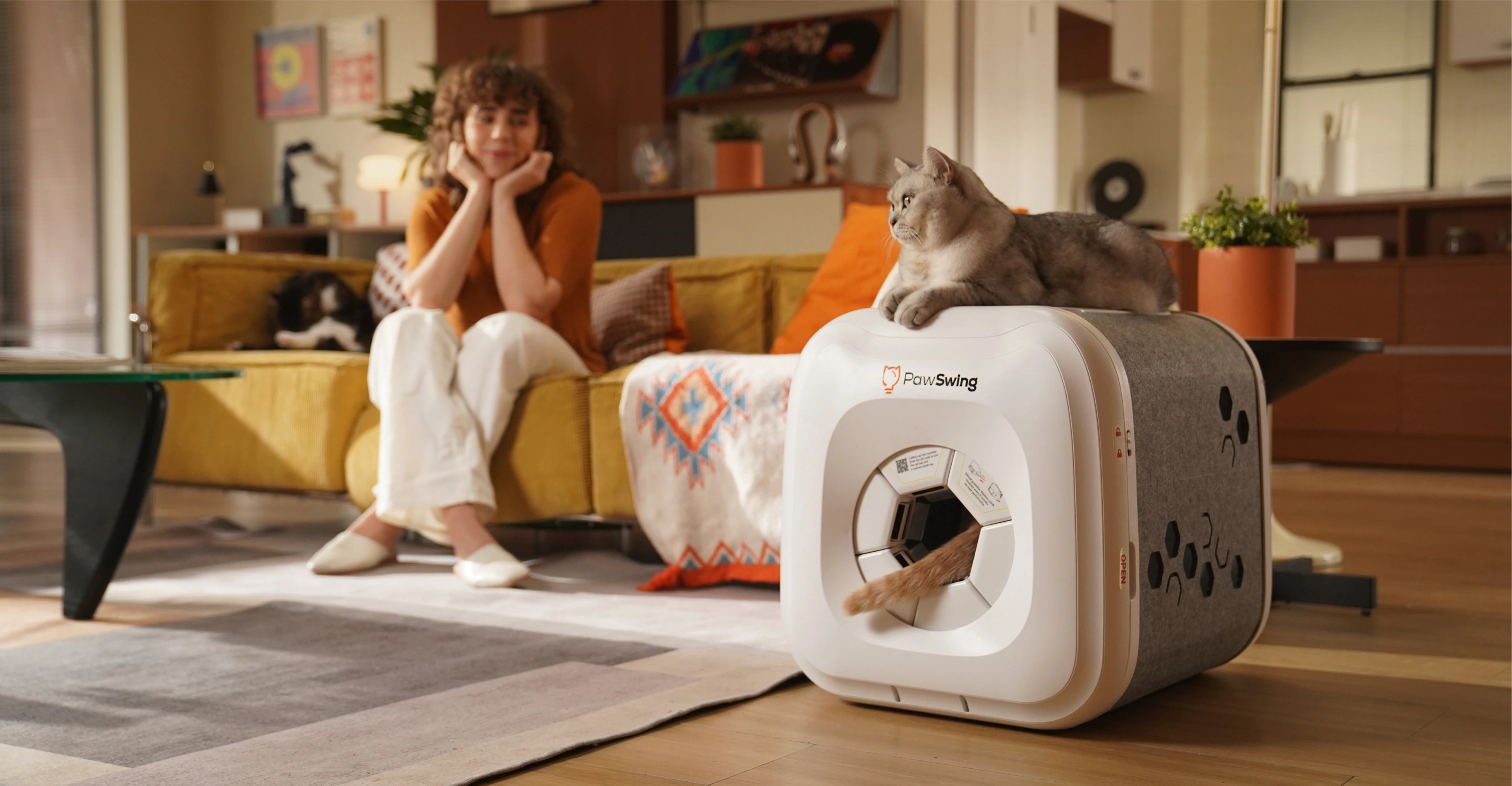 Başka bir kedinin kuyruğu içeriden bakarken, PawSwing® neo kendi kendini temizleyen kedi evinde dinlenen bir kedi
